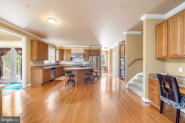 kitchen with stainless steel appliances, under cabinet range hood, a kitchen bar, light wood-type flooring, and brown cabinets