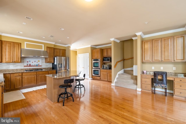 kitchen featuring appliances with stainless steel finishes, range hood, a breakfast bar area, light wood-type flooring, and crown molding