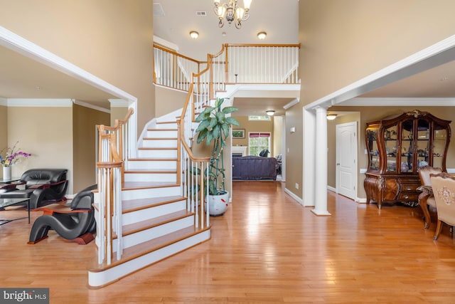 entryway with decorative columns, a high ceiling, wood finished floors, stairway, and crown molding