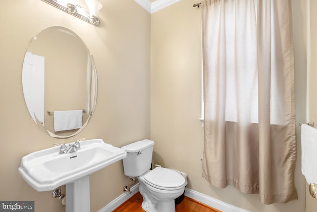 half bath featuring baseboards, toilet, wood finished floors, crown molding, and a sink