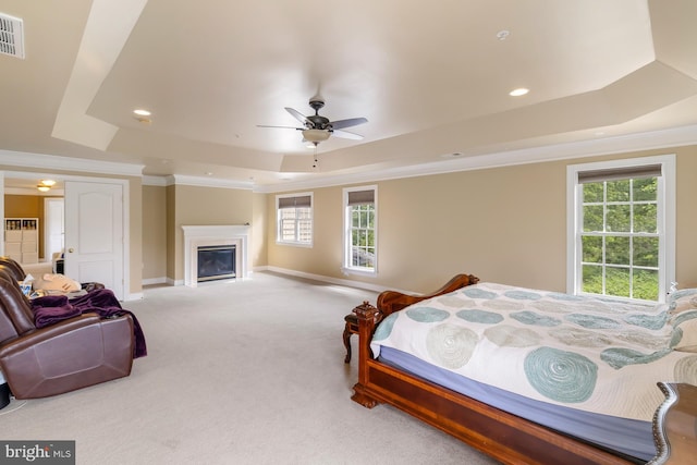 bedroom with a tray ceiling, carpet floors, multiple windows, a glass covered fireplace, and crown molding