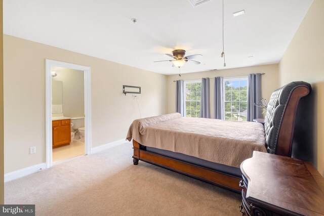 bedroom with light carpet, ensuite bathroom, baseboards, and a ceiling fan