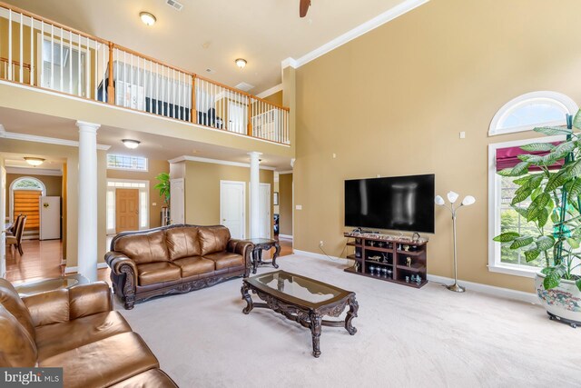 carpeted living area with decorative columns, a high ceiling, baseboards, crown molding, and ceiling fan