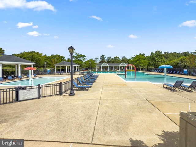 community pool with a gazebo, fence, view of wooded area, and a patio