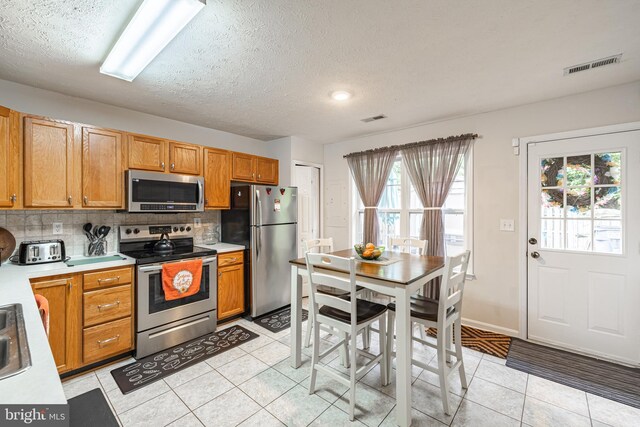 9910 Warwick Pl, Fredericksburg, VA 22408 - kitchen featuring stainless steel appliances, light tile patterned flooring, backsplash, light countertops, and a textured ceiling