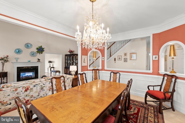 dining space featuring light colored carpet, ornamental molding, wainscoting, a glass covered fireplace, and stairway
