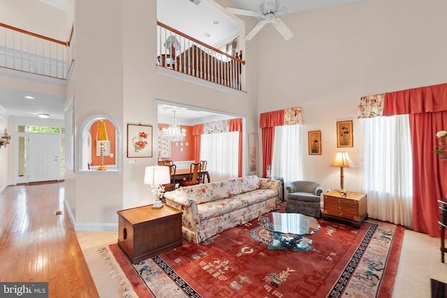 living room with a towering ceiling, a chandelier, hardwood / wood-style floors, a ceiling fan, and baseboards