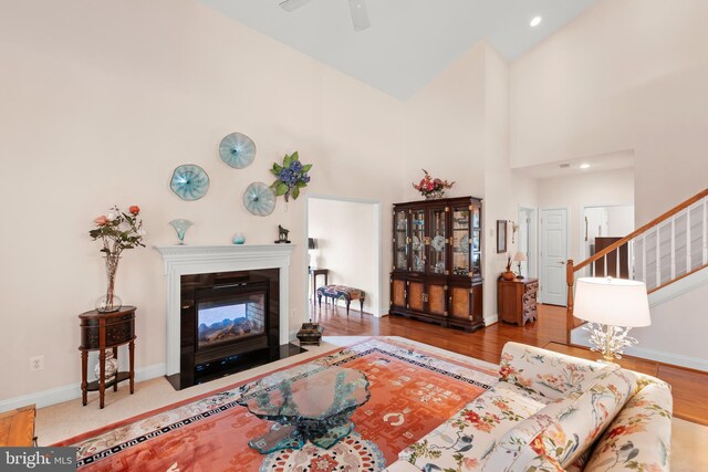 living area featuring a ceiling fan, wood finished floors, stairs, baseboards, and a high ceiling