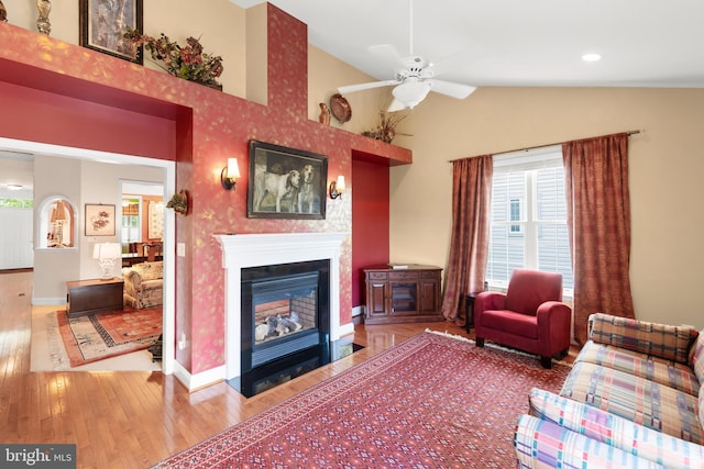 living area featuring wood finished floors, plenty of natural light, ceiling fan, a fireplace with flush hearth, and lofted ceiling