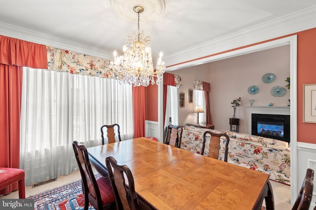 carpeted dining area with a chandelier, plenty of natural light, a glass covered fireplace, and crown molding