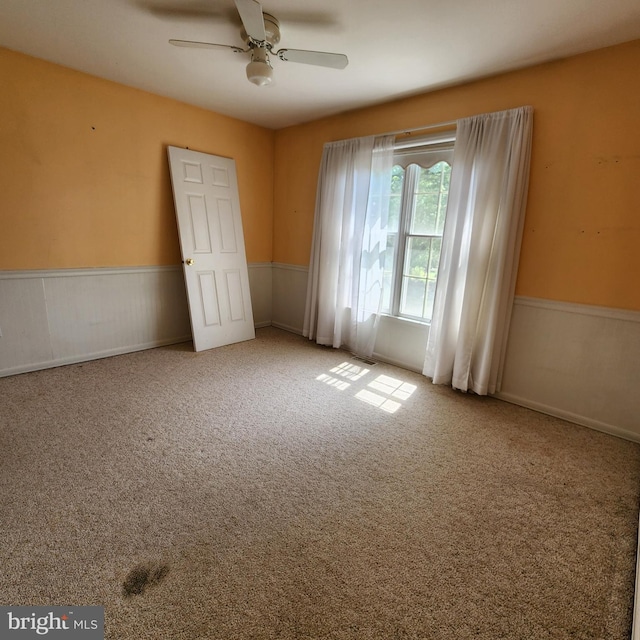 carpeted empty room featuring ceiling fan and a wainscoted wall