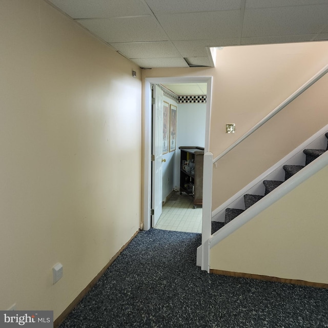 hallway with a paneled ceiling, stairway, and baseboards