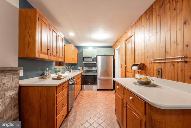 kitchen featuring stainless steel appliances, light countertops, a sink, wood walls, and brown cabinetry