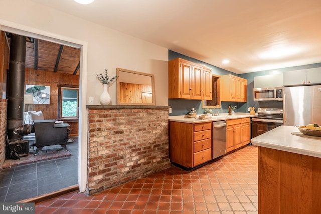 kitchen with appliances with stainless steel finishes, light countertops, wooden walls, tile patterned flooring, and a wood stove