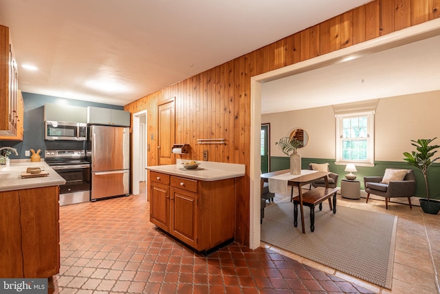 kitchen featuring appliances with stainless steel finishes, wooden walls, light countertops, brown cabinetry, and a sink