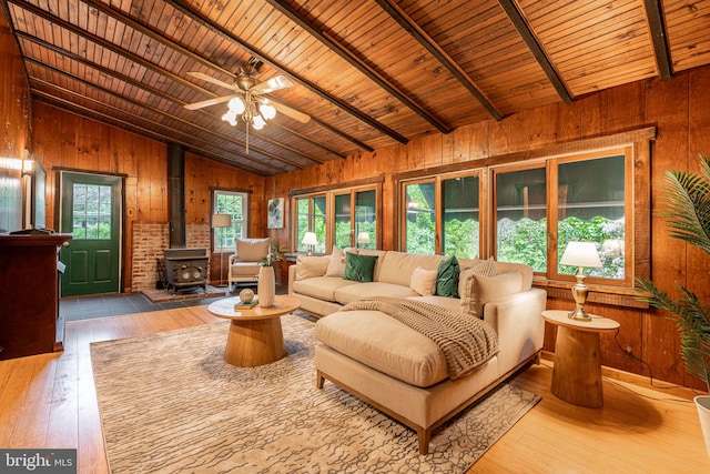 living area featuring wooden walls, a wood stove, wood-type flooring, wood ceiling, and a ceiling fan