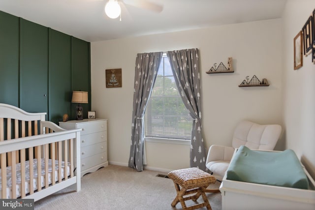 bedroom with a crib, light colored carpet, baseboards, and a ceiling fan