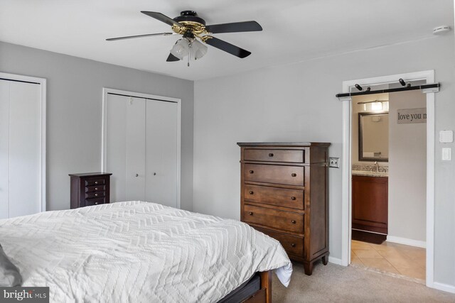 bedroom with light colored carpet, multiple closets, baseboards, a sink, and ensuite bath