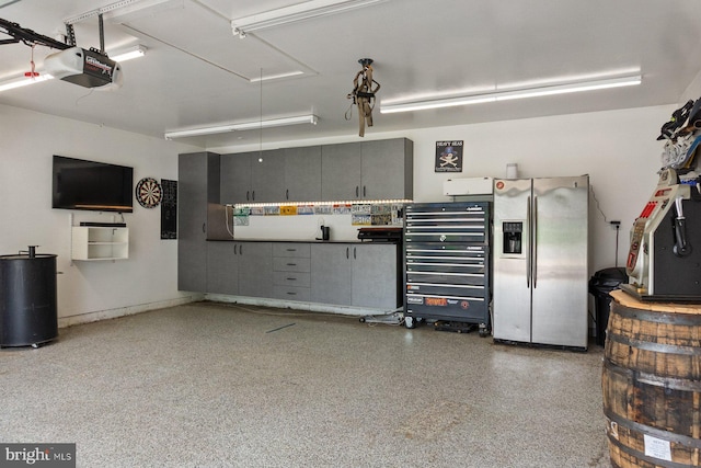 garage with stainless steel refrigerator with ice dispenser and a garage door opener