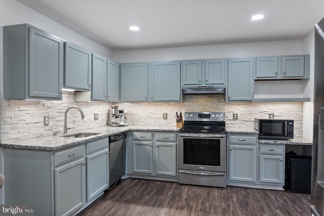 kitchen featuring appliances with stainless steel finishes, a sink, under cabinet range hood, dark wood finished floors, and light stone countertops