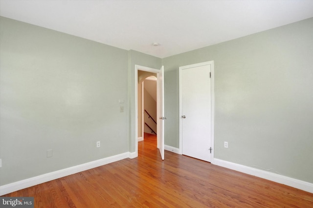 empty room featuring baseboards, light wood-type flooring, and arched walkways