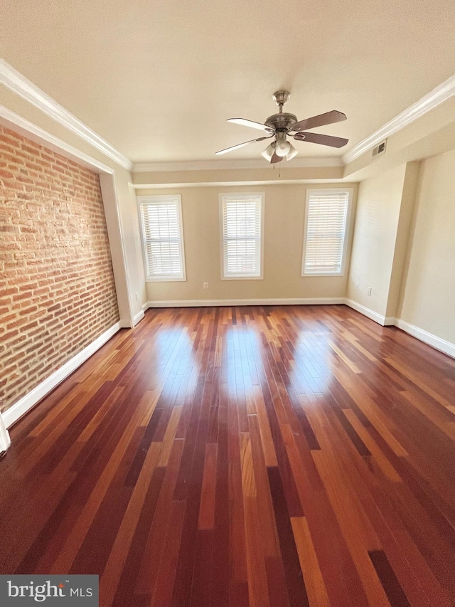 unfurnished room featuring a ceiling fan, brick wall, wood finished floors, baseboards, and ornamental molding