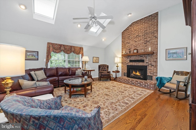 living area featuring a skylight, vaulted ceiling, wood finished floors, a fireplace, and a ceiling fan