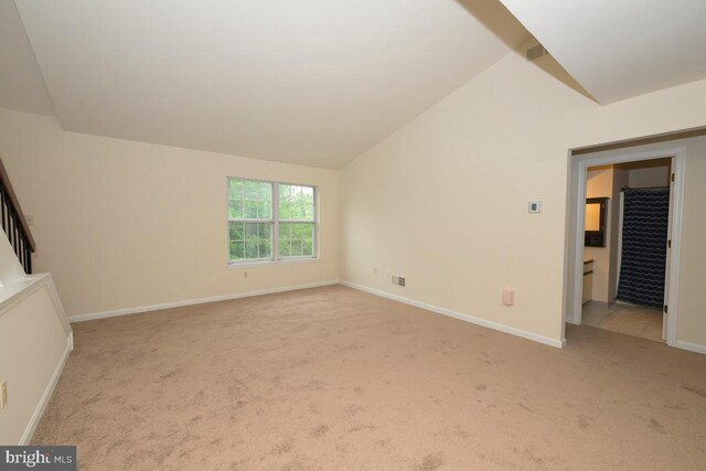 carpeted empty room featuring vaulted ceiling and baseboards