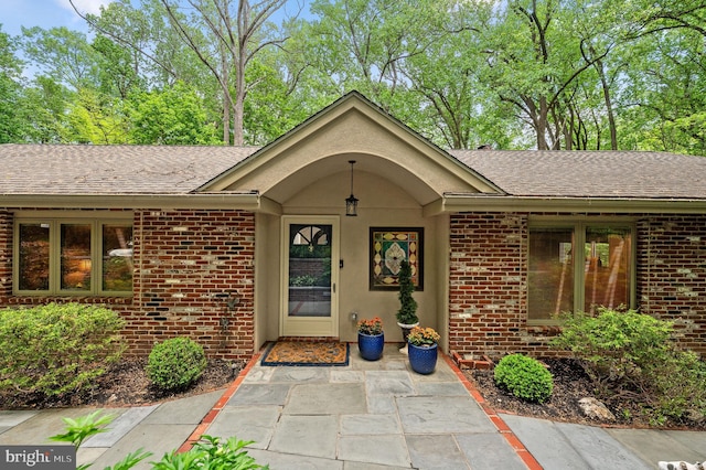 property entrance with brick siding, a shingled roof, and a patio