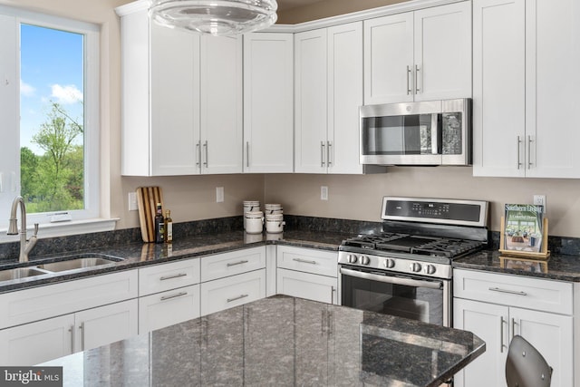 kitchen with stainless steel appliances, white cabinetry, a sink, and dark stone counters