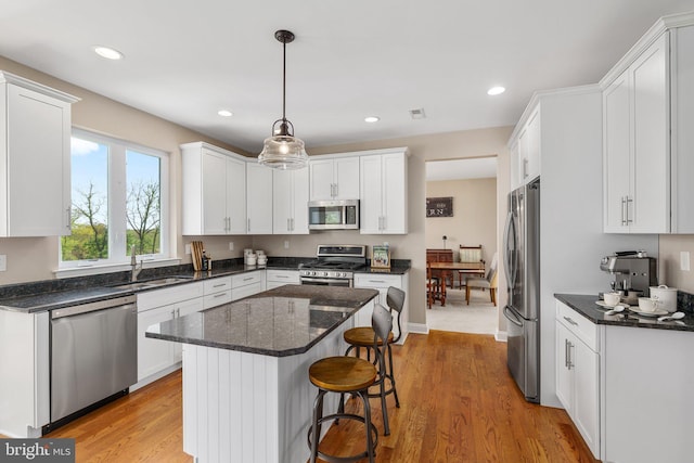 kitchen with appliances with stainless steel finishes, a sink, white cabinets, light wood-style floors, and a kitchen island