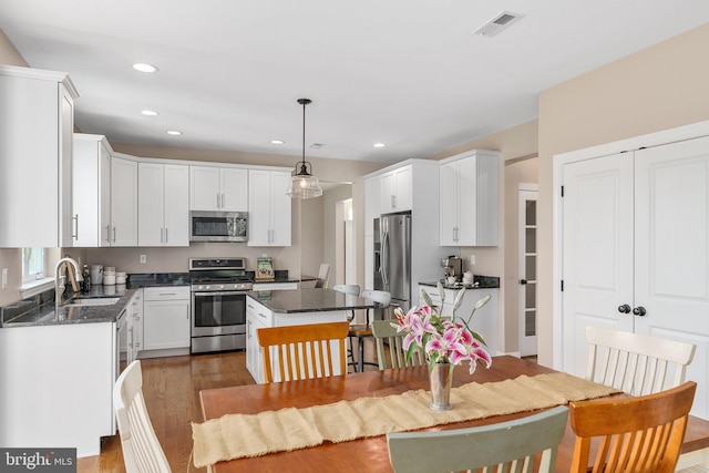 kitchen featuring appliances with stainless steel finishes, a sink, wood finished floors, a center island, and white cabinets