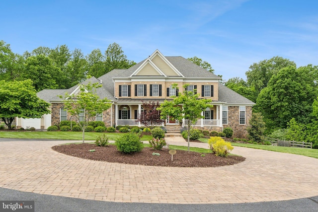 view of front facade featuring curved driveway, covered porch, stone siding, and roof with shingles