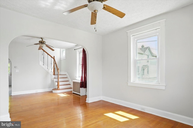 spare room with arched walkways, a ceiling fan, a textured ceiling, stairway, and light wood-type flooring