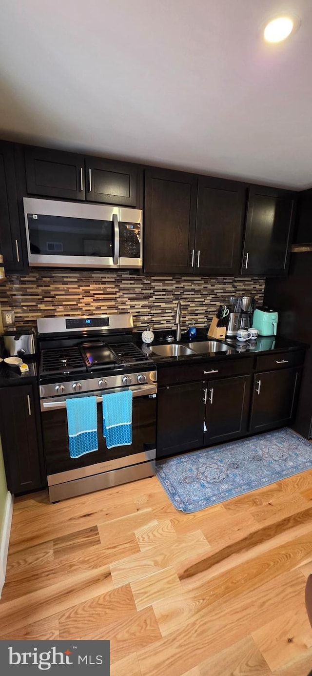 kitchen with stainless steel appliances, a sink, tasteful backsplash, and dark countertops