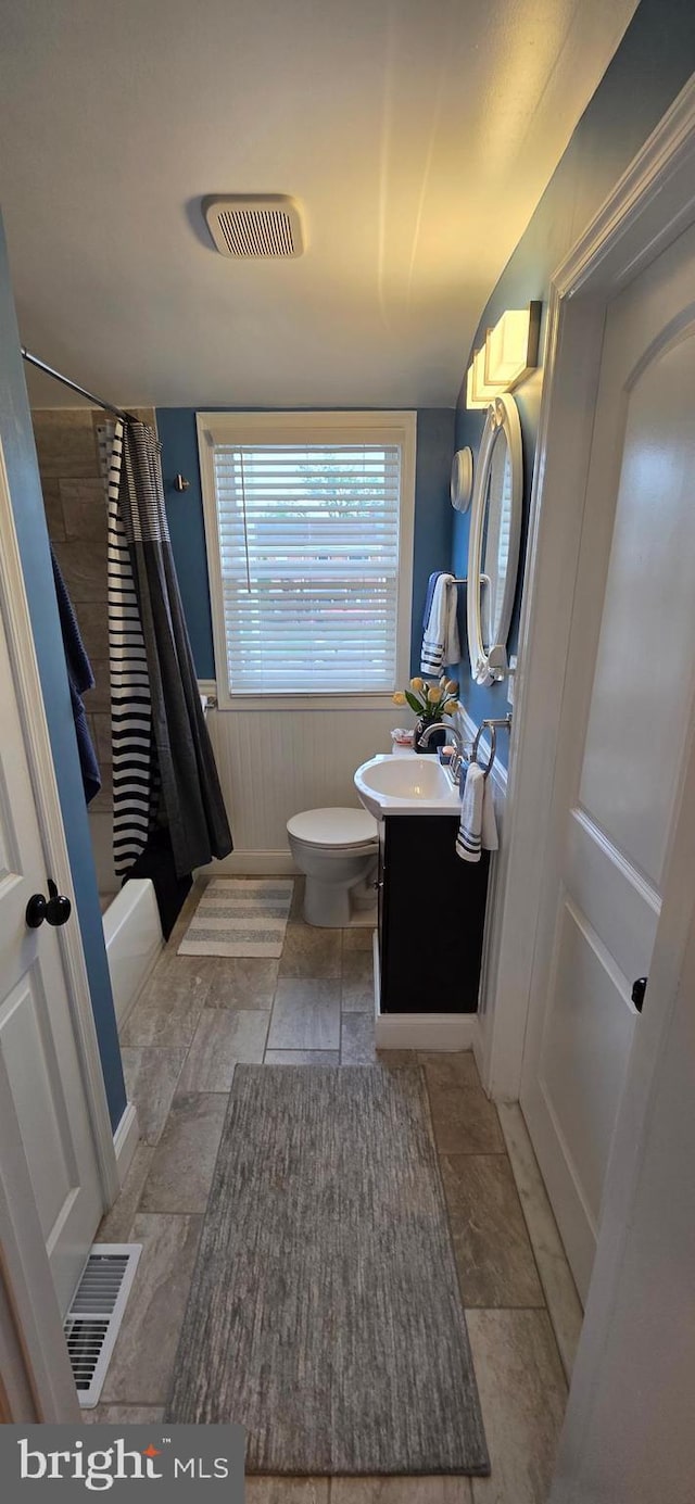 full bathroom featuring toilet, vanity, shower / tub combo, and wainscoting
