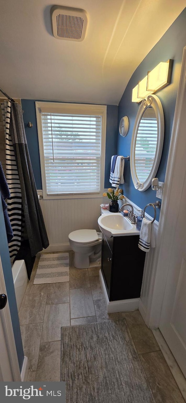 bathroom with toilet, vanity, wainscoting, and lofted ceiling