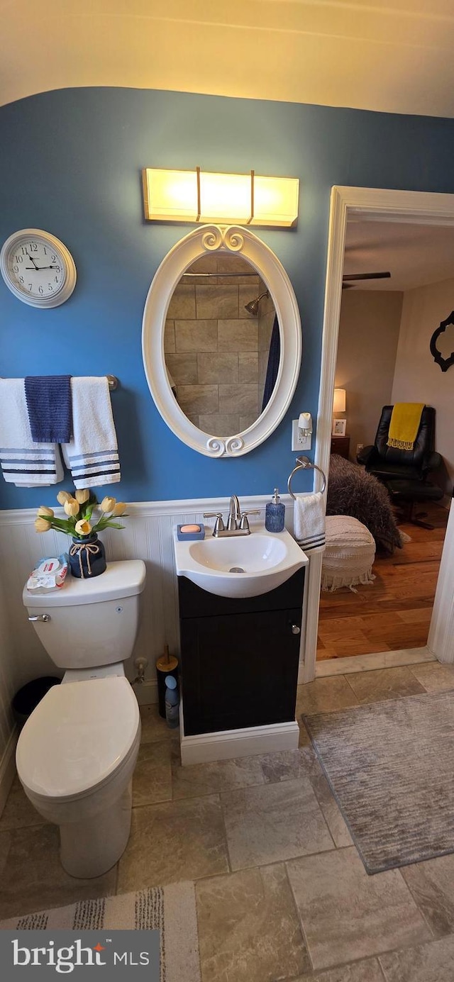 bathroom featuring vanity, a wainscoted wall, toilet, and stone finish flooring
