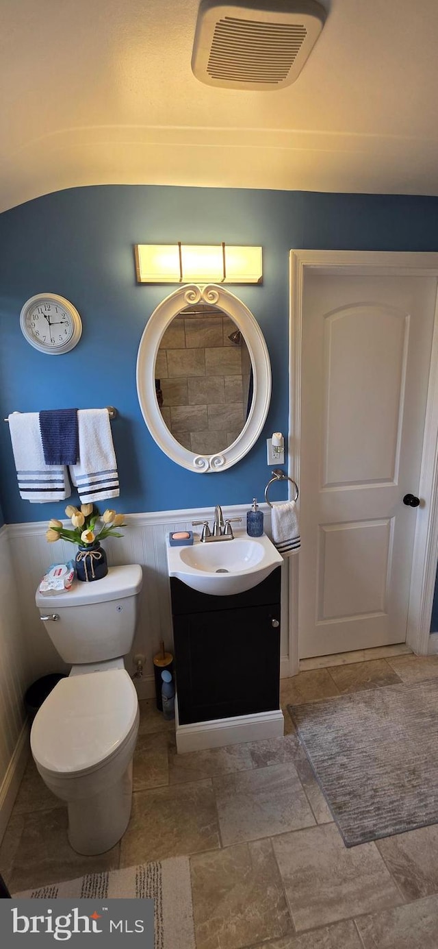 bathroom with vanity, wainscoting, toilet, and stone finish floors