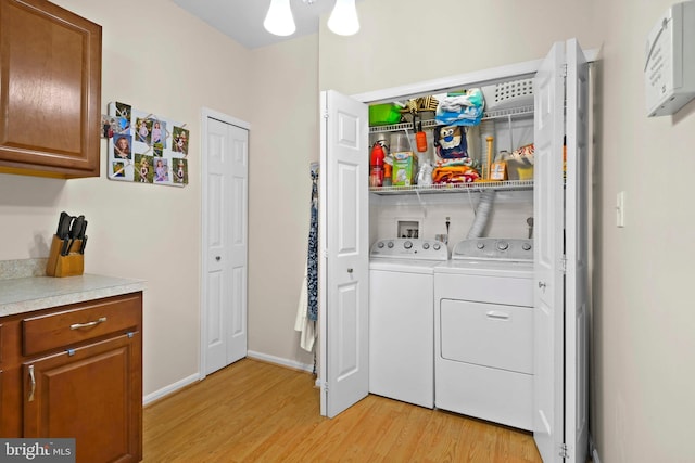 clothes washing area featuring washing machine and dryer, light wood finished floors, and baseboards