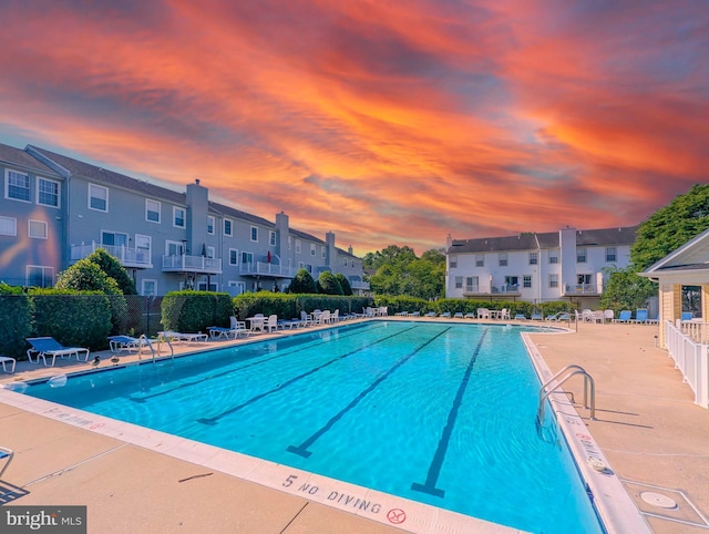 pool at dusk featuring a community pool, fence, a residential view, and a patio