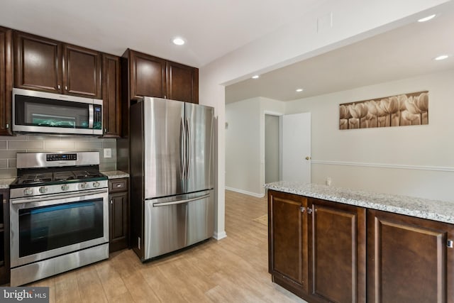 7879 Wintercress Ln, Springfield, VA 22152 - kitchen with appliances with stainless steel finishes, dark brown cabinets, light wood-style flooring, backsplash, and light stone counters