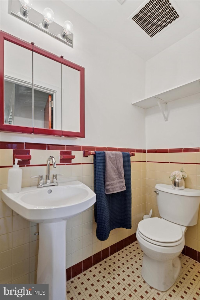half bathroom featuring tile walls, toilet, and a wainscoted wall
