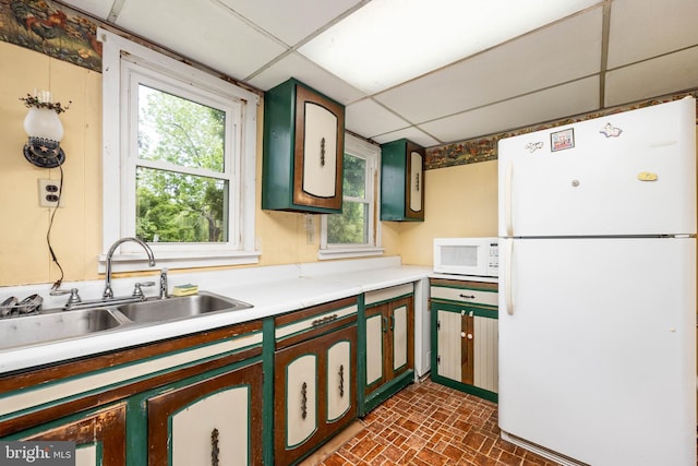 kitchen with white appliances, a drop ceiling, a sink, light countertops, and healthy amount of natural light
