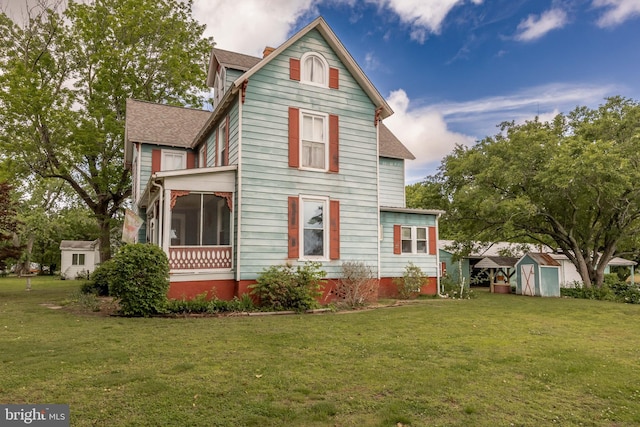 rear view of property with a storage unit, a shingled roof, a sunroom, and a yard