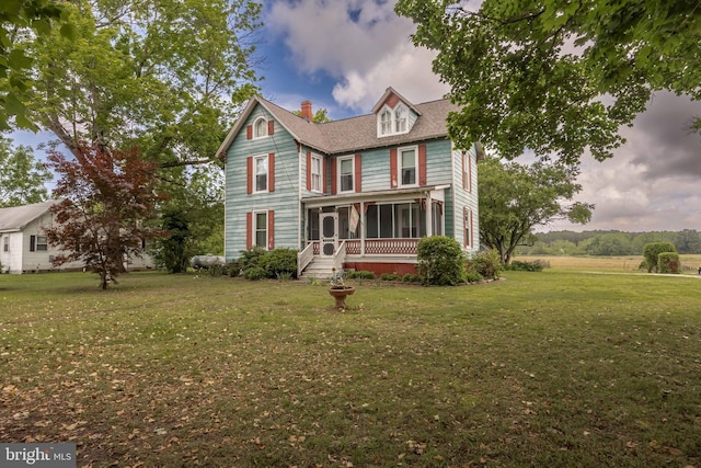 victorian-style house with a sunroom, a chimney, and a front yard