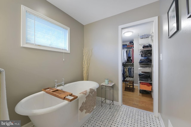 full bathroom with a soaking tub, baseboards, tile patterned floors, and a walk in closet