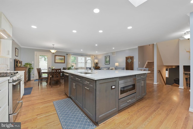 kitchen featuring appliances with stainless steel finishes, a sink, light countertops, light wood-style flooring, and a center island with sink