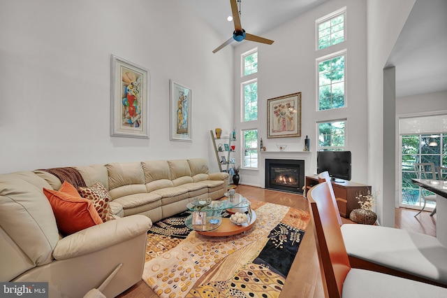 living room with a ceiling fan, wood finished floors, a high ceiling, and a glass covered fireplace