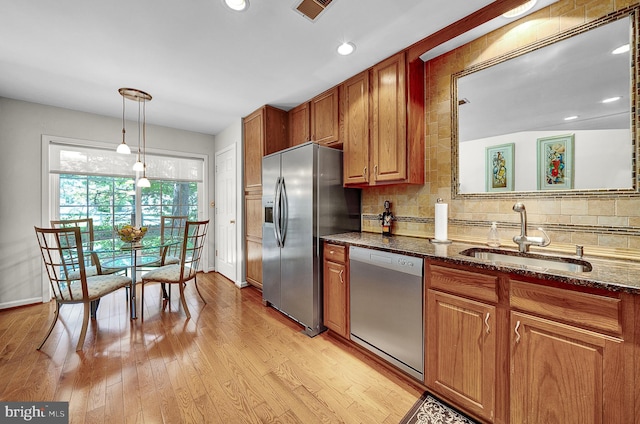 kitchen featuring stainless steel appliances, a sink, decorative backsplash, brown cabinets, and dark stone counters